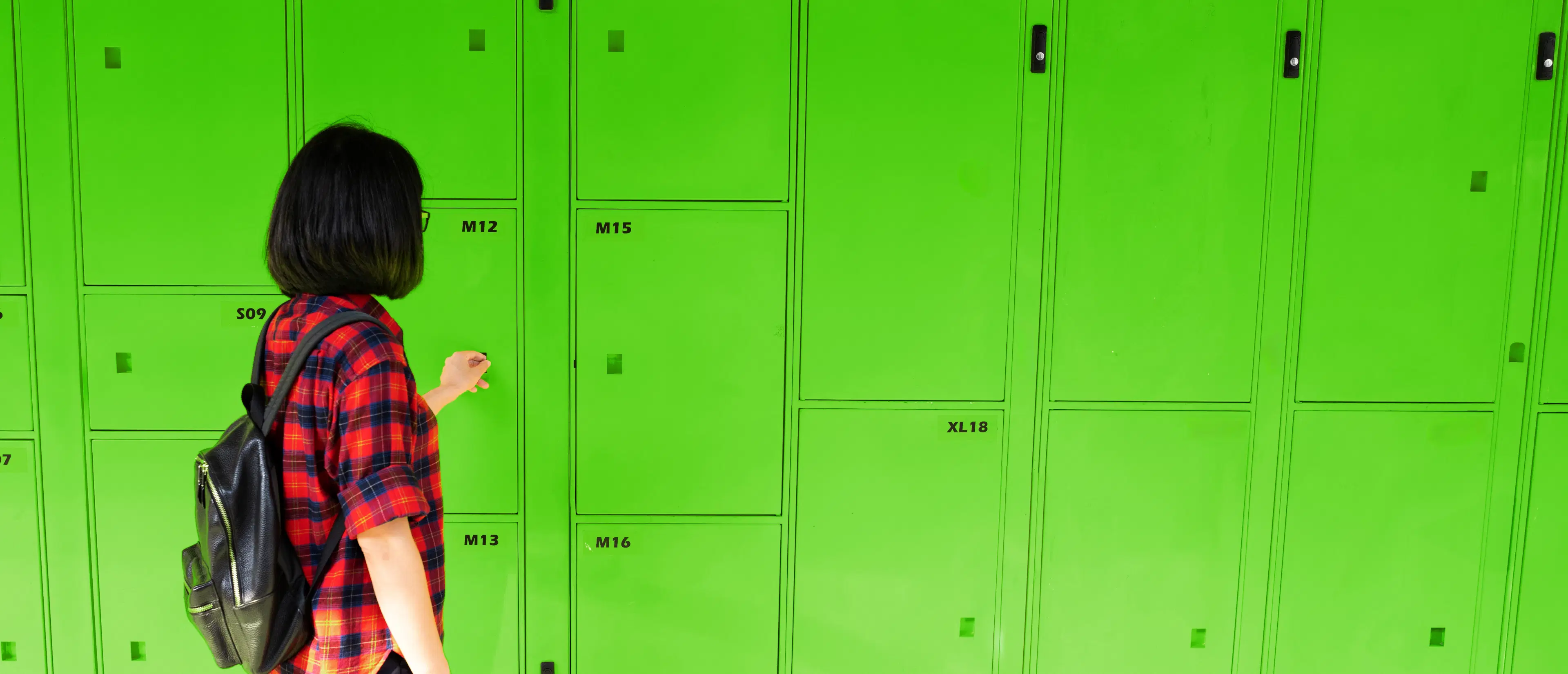 A person storing luggage in a green locker facility in Australia.
